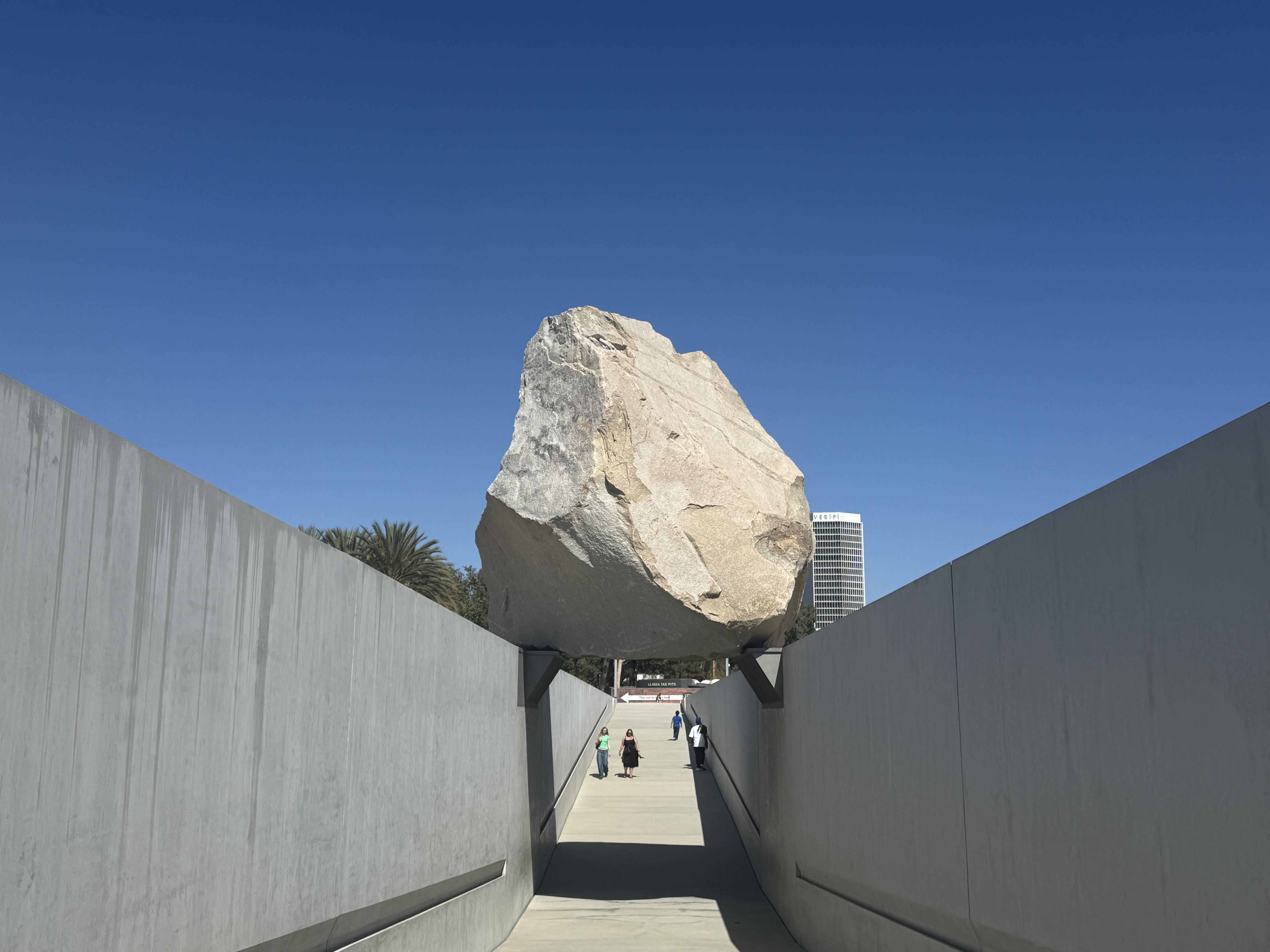 A large-scale public art installation featuring a balanced boulder over a concrete walkway.